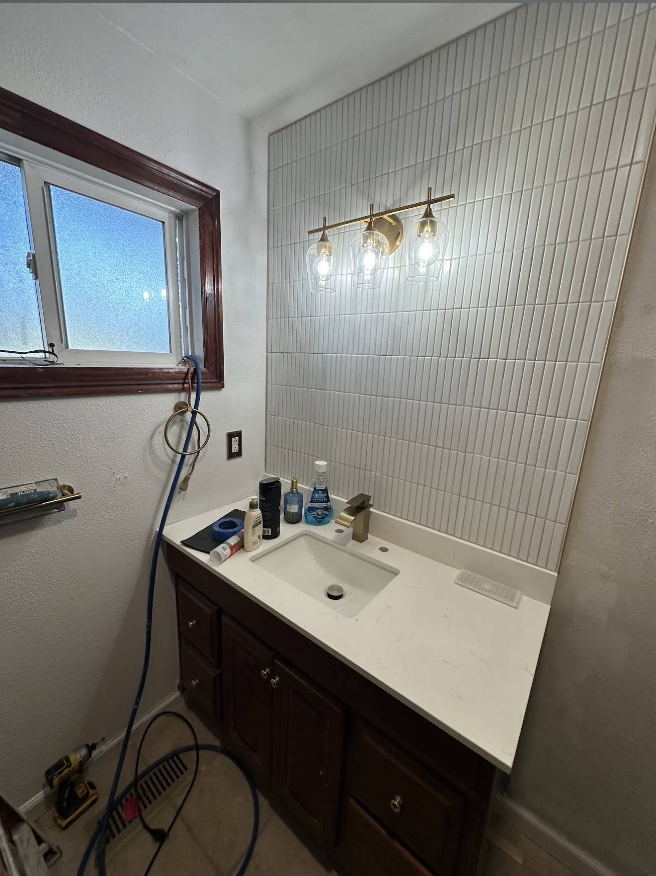 A finished master bath remodel by Cazares — stacked white tile, quartz vanity, brass triple-pendant lighting.